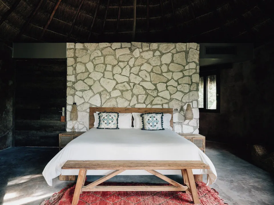 Bedroom with stone feature wall and king bed under a palapa roof at Nômade Temple Tulum