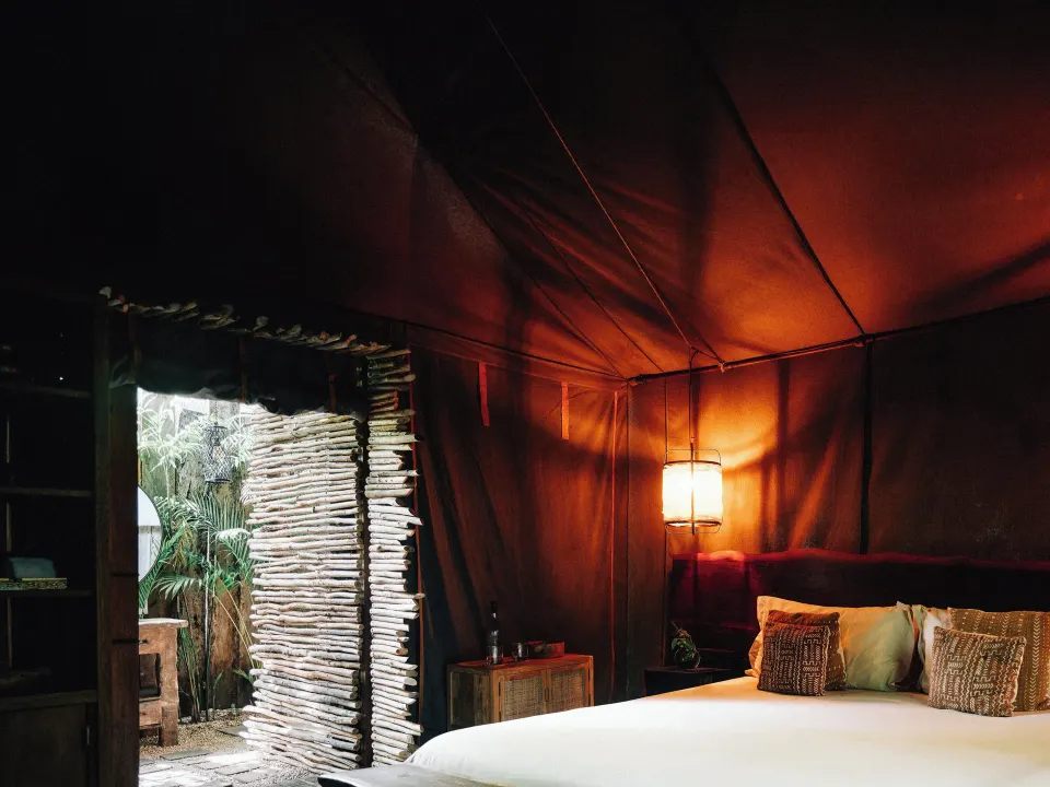 Tent-style bedroom with warm lantern light and an open woven screen at Nômade Temple Tulum