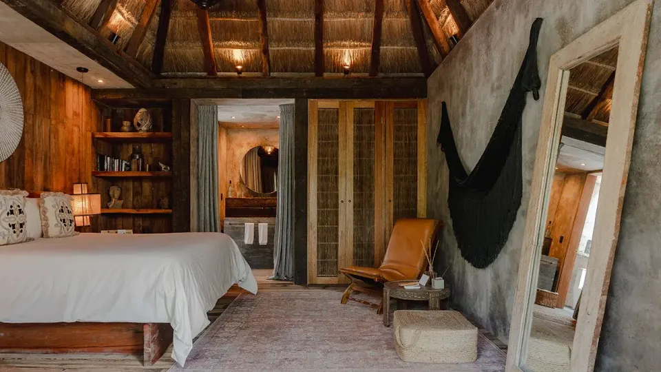 Spacious suite interior with king bed, wooden furniture and thatched ceiling at Nômade Temple Tulum