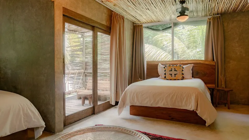 Twin beds next to sliding glass doors opening to a deck and palms at Nômade Temple Tulum