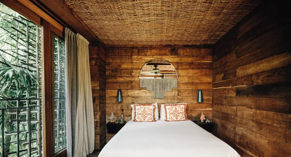 Wood-paneled bedroom with bed and woven ceiling at Nômade Temple Tulum