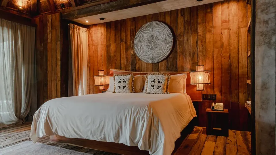 King bed against a wooden plank accent wall with bedside lamps at Nômade Temple Tulum