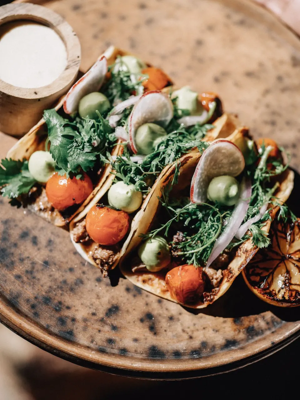 Three small tacos garnished with herbs and radish slices at Nômade Temple Tulum.