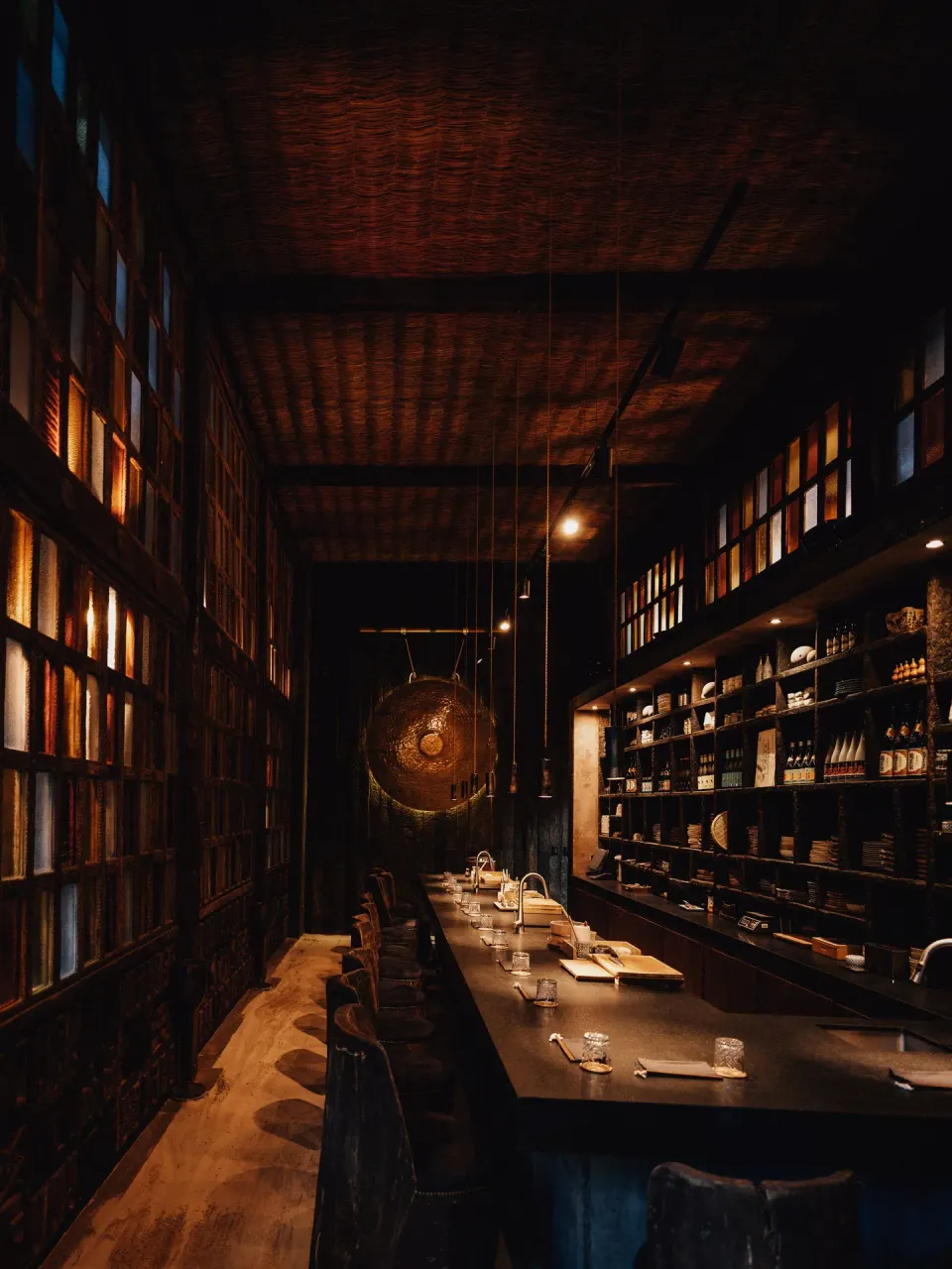 Intimate dimly lit long dining counter with shelves and a gong at Nômade Temple Tulum