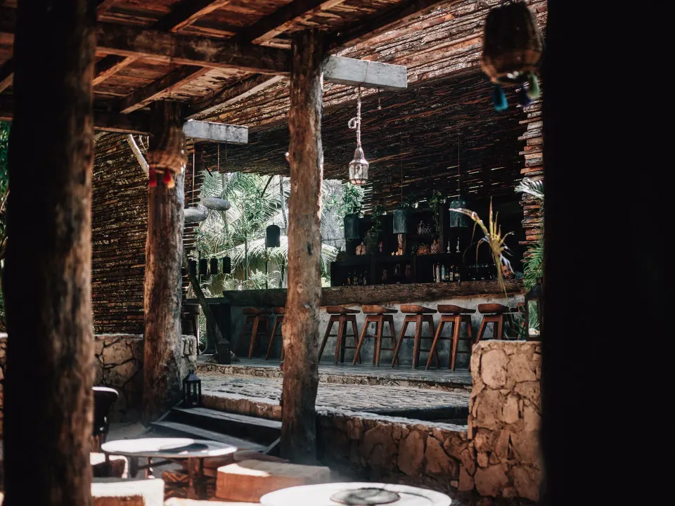 Rustic open-air bar with wooden beams and stools at Nômade Temple Tulum.