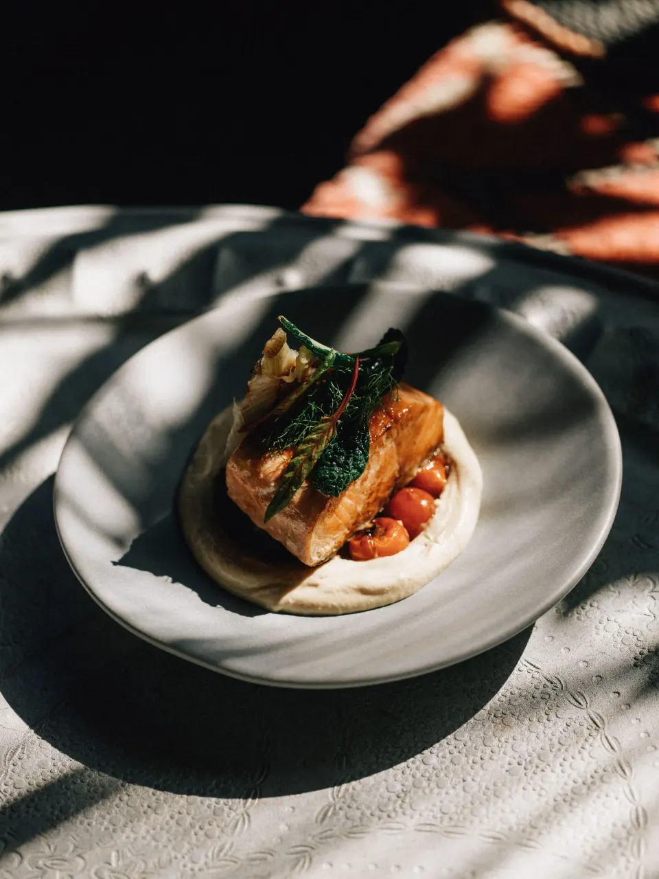 Plated fish with greens and tomatoes on a white dish at Nômade Temple Tulum.