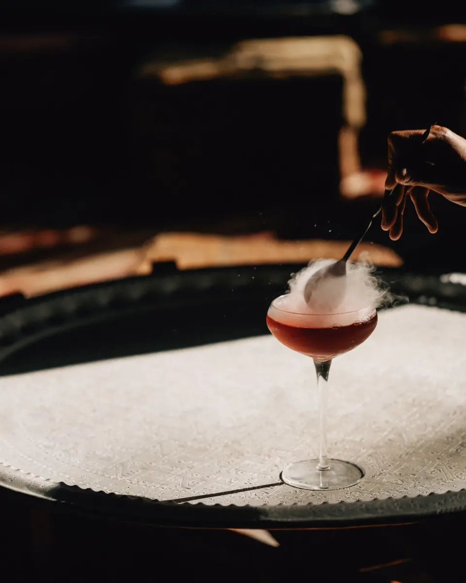 A plated cocktail emitting smoke on a metal tray at Nômade Temple Tulum.