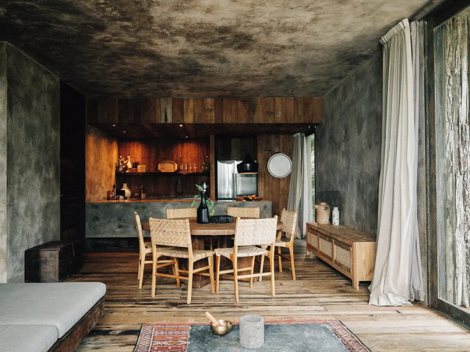 Dining table and kitchenette in a suite with wood floors at Nômade Temple Tulum