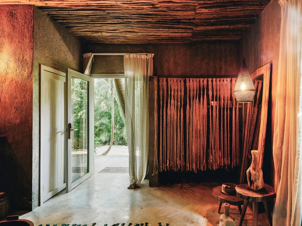 Deluxe Room entrance at Nômade Temple Tulum showing the doorway to the garden and a woven curtain divider