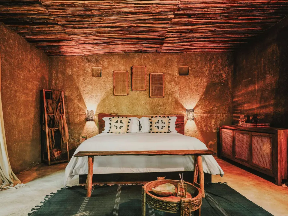 King bed in a rustic Deluxe Room, Garden View at Nômade Temple Tulum with textured walls and ceiling