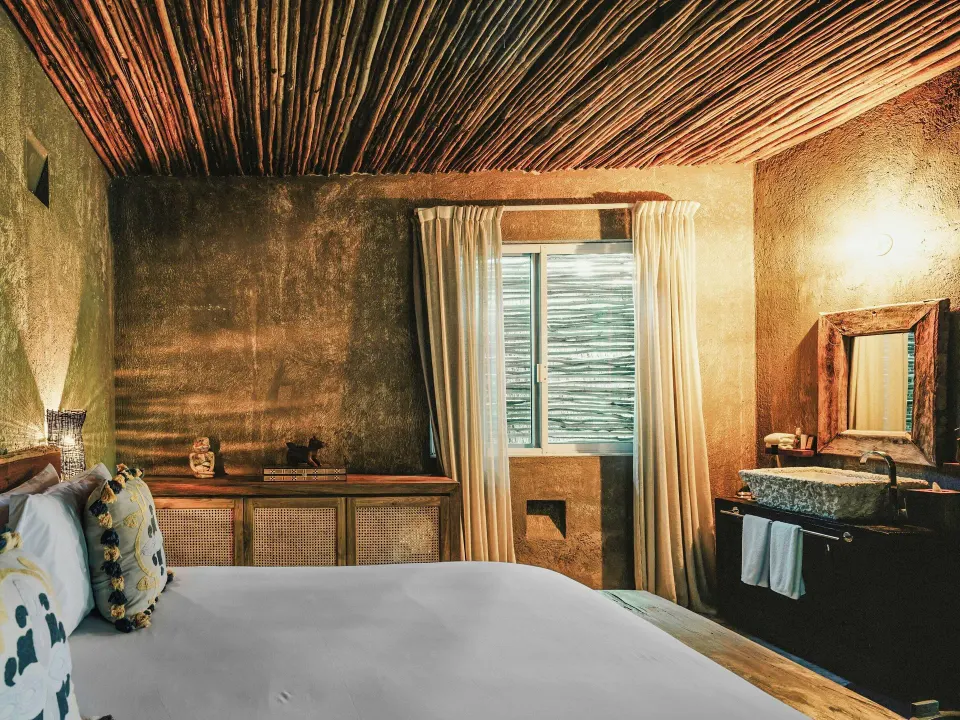 Side view of the Deluxe Room, Garden View at Nômade Temple Tulum showing the bed, window and vanity sink