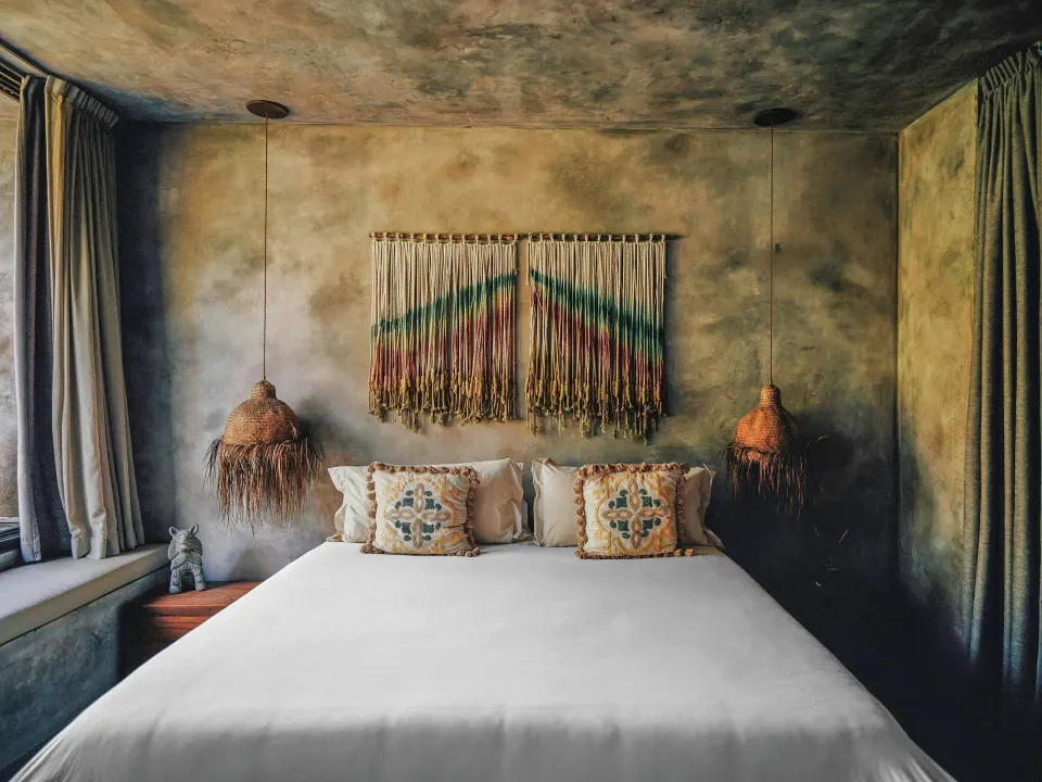 Front view of a king bed with woven wall hanging in a Deluxe Room at Nômade Temple Tulum