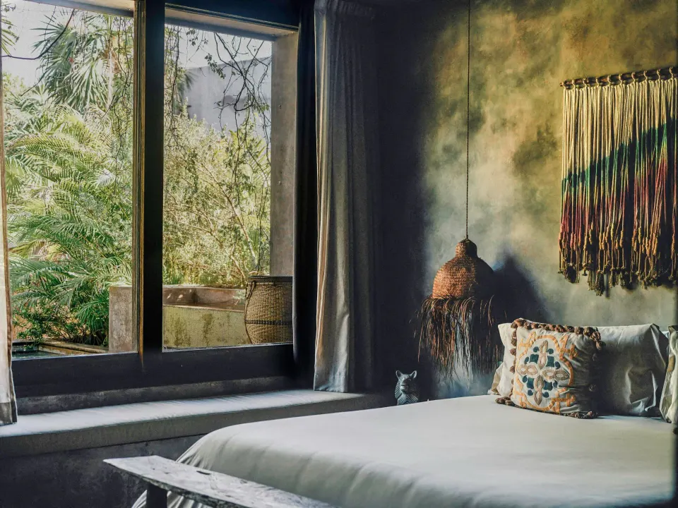 Side view of the bed and large window showing jungle foliage in a Deluxe Room at Nômade Temple Tulum