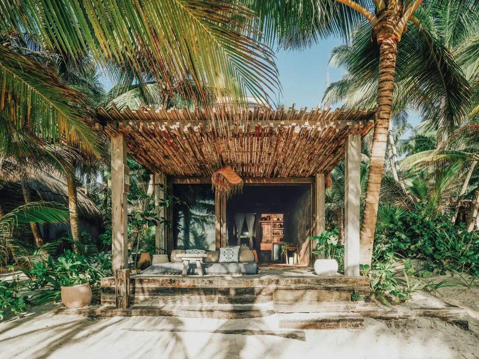 Exterior of an ocean-view bungalow with shaded front terrace and palms at Nômade Temple Tulum