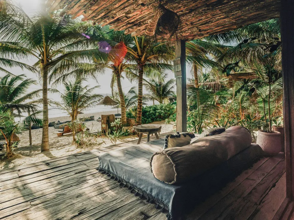 Oceanfront room deck with daybed and palm trees looking toward the sea at Nômade Temple Tulum