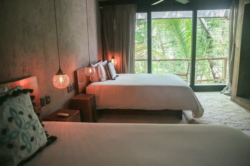 Deluxe room showing single bed and balcony door framed by tropical plants at Nômade Temple Tulum