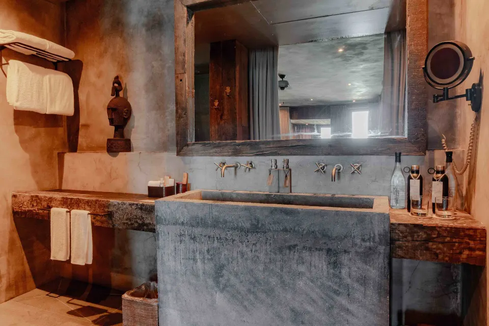 Close-up of a sculpted stone sink and mirror in a Suite Ocean View at Nômade Temple Tulum.