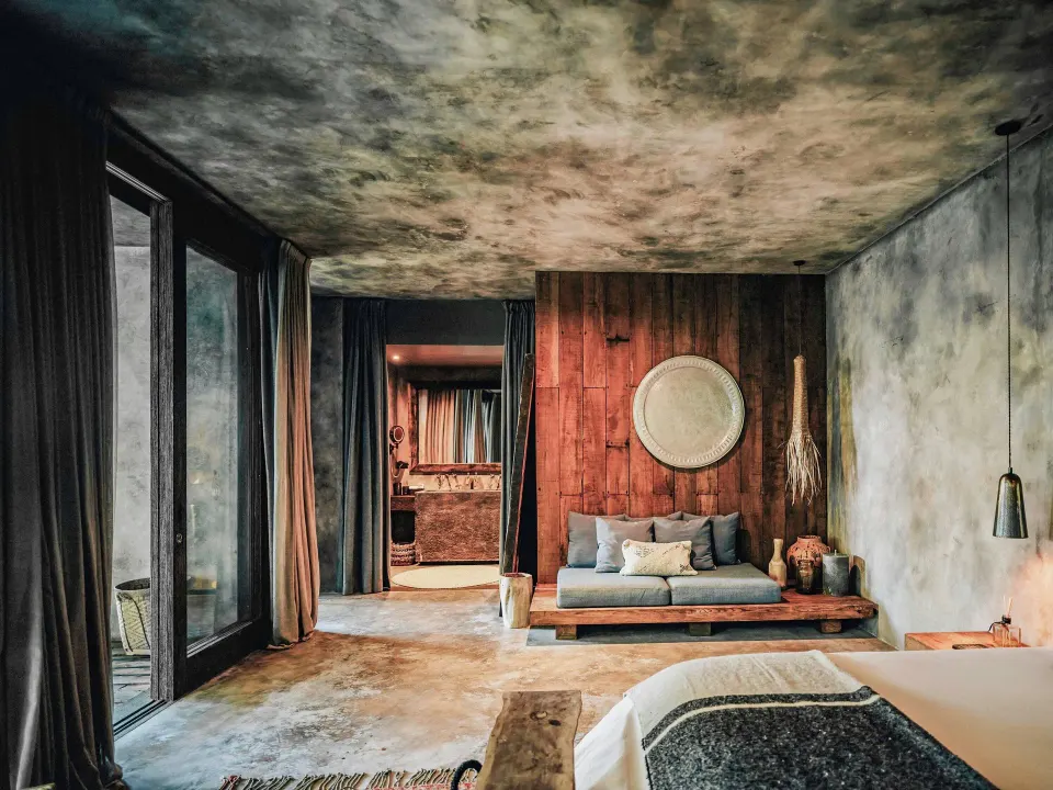 Suite interior with king bed, wood-accent wall and sofa at Nômade Temple Tulum