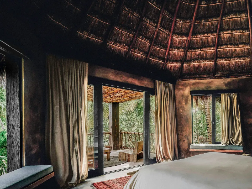 Palapa-roofed bedroom interior with sliding doors and drapes in a Superior Room Beach View at Nômade Temple Tulum