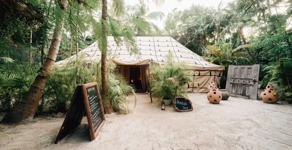 Exterior of a large canvas tent entrance surrounded by palms at Nômade Temple Tulum.
