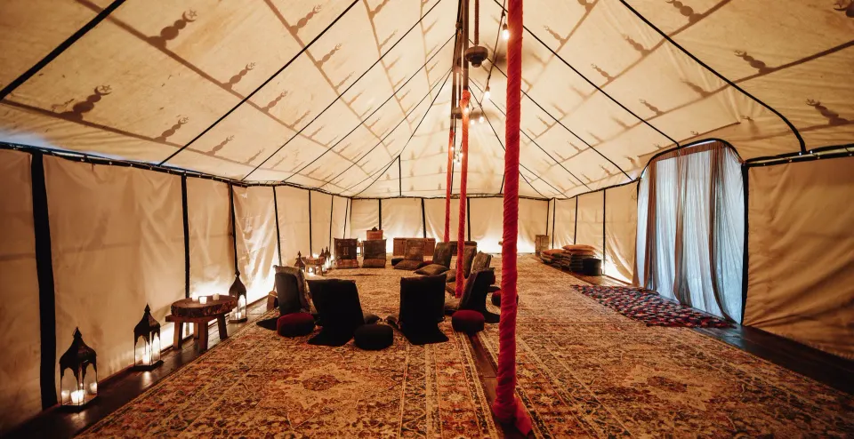 Interior of a large tent with rugs, low seating and lanterns at Nômade Temple Tulum.