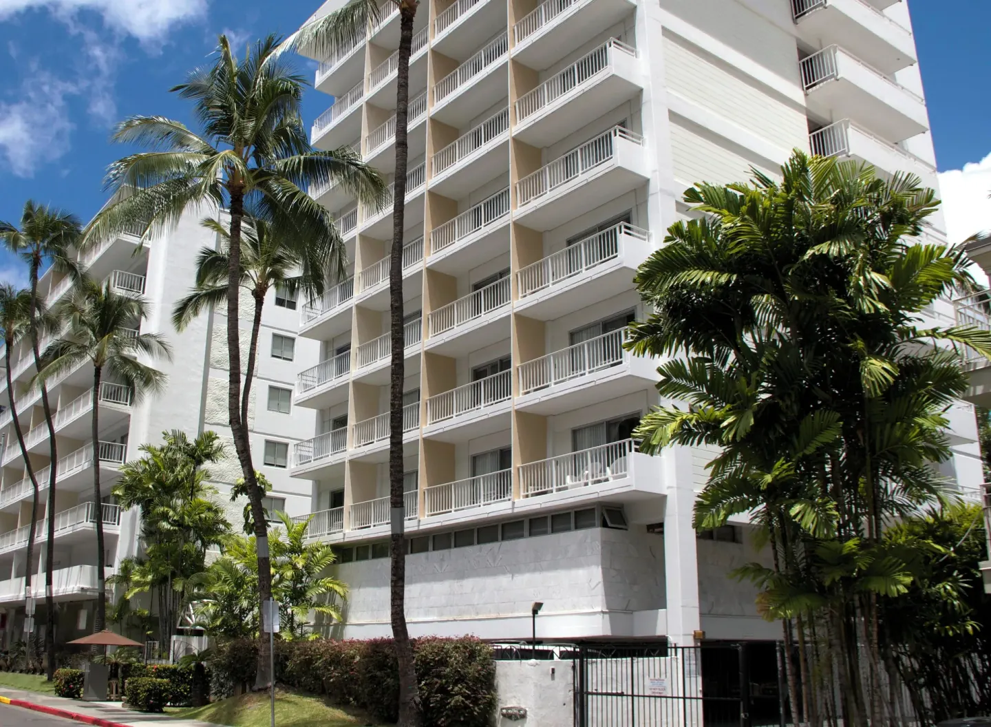 White hotel tower with balconies and palm trees at Oasis Hotel Waikiki.