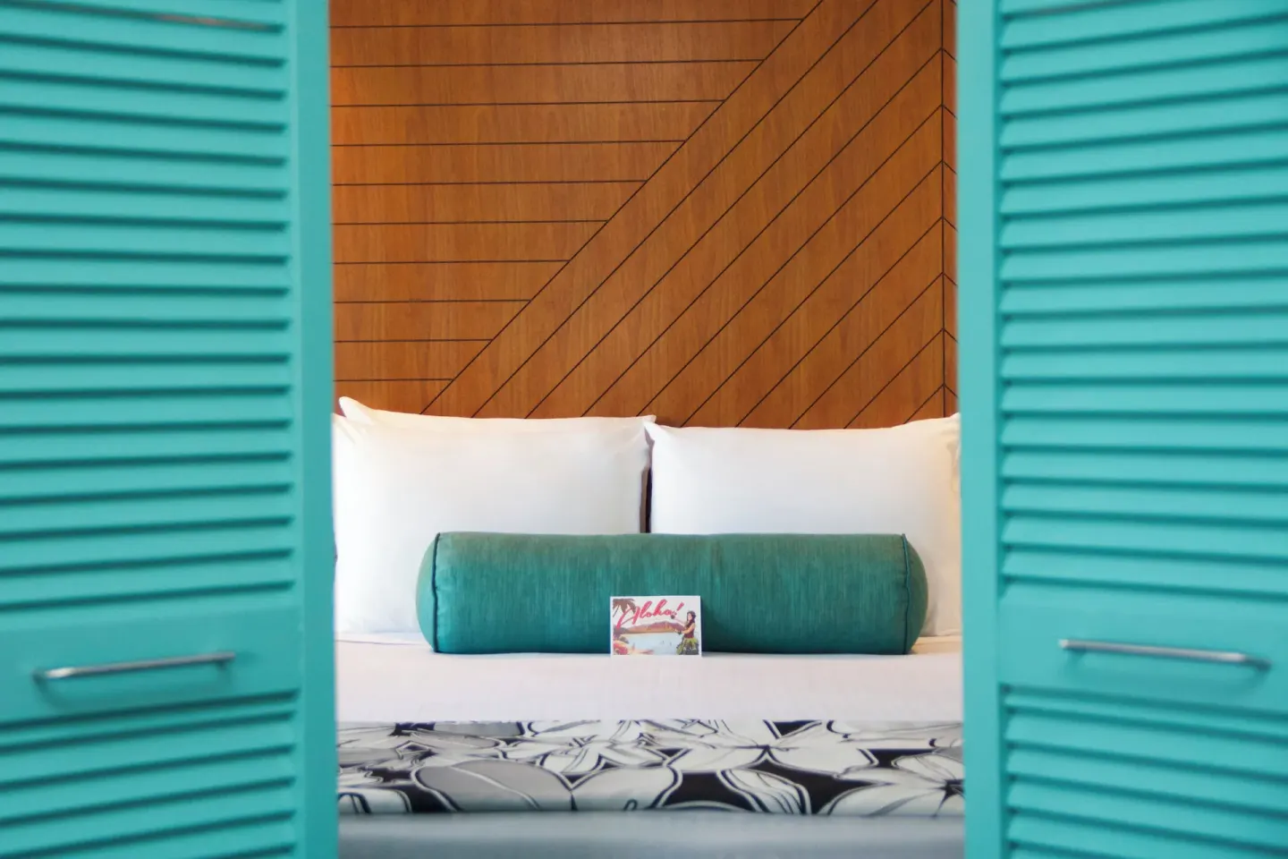 Guest room bed framed by turquoise louvered doors at Oasis Hotel Waikiki.