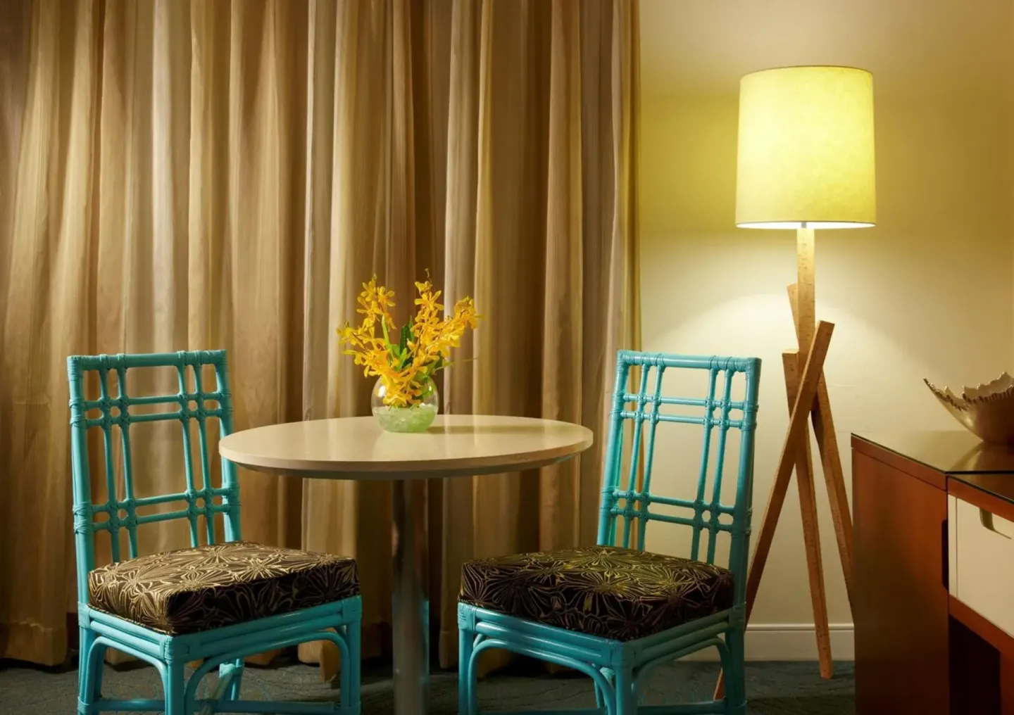 Round table, teal chairs, and floor lamp in a guest room at Oasis Hotel Waikiki.