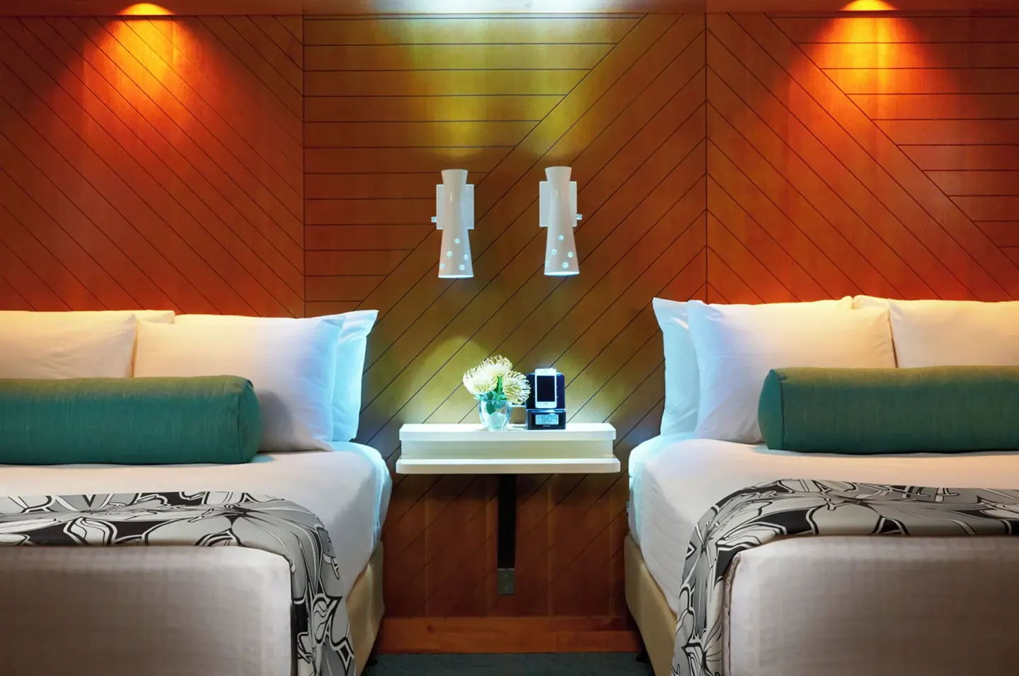 Two beds with teal bolsters and wood panel headboard at Oasis Hotel Waikiki.