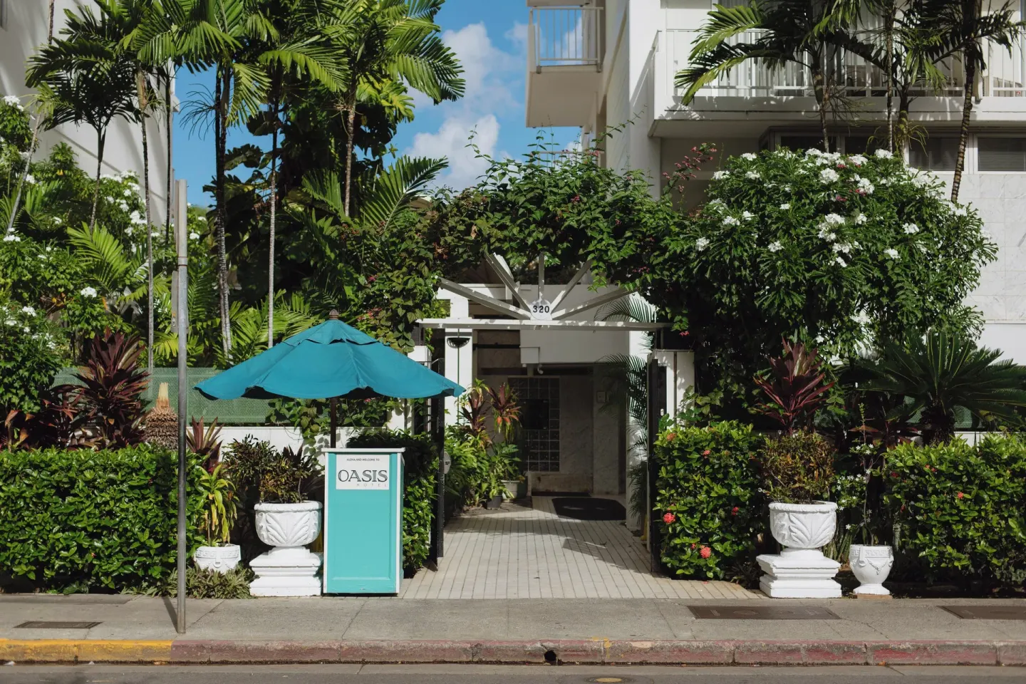 Landscaped walkway entrance with a teal umbrella at Oasis Hotel Waikiki.