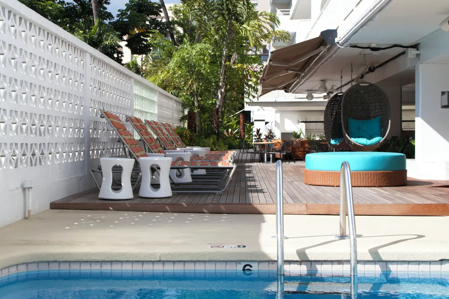 Pool deck with lounge chairs and hanging egg chair at Oasis Hotel Waikiki.