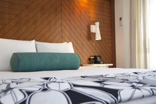 Close-up of a Club Suite bed with teal bolster and wood headboard at Oasis Hotel Waikiki.