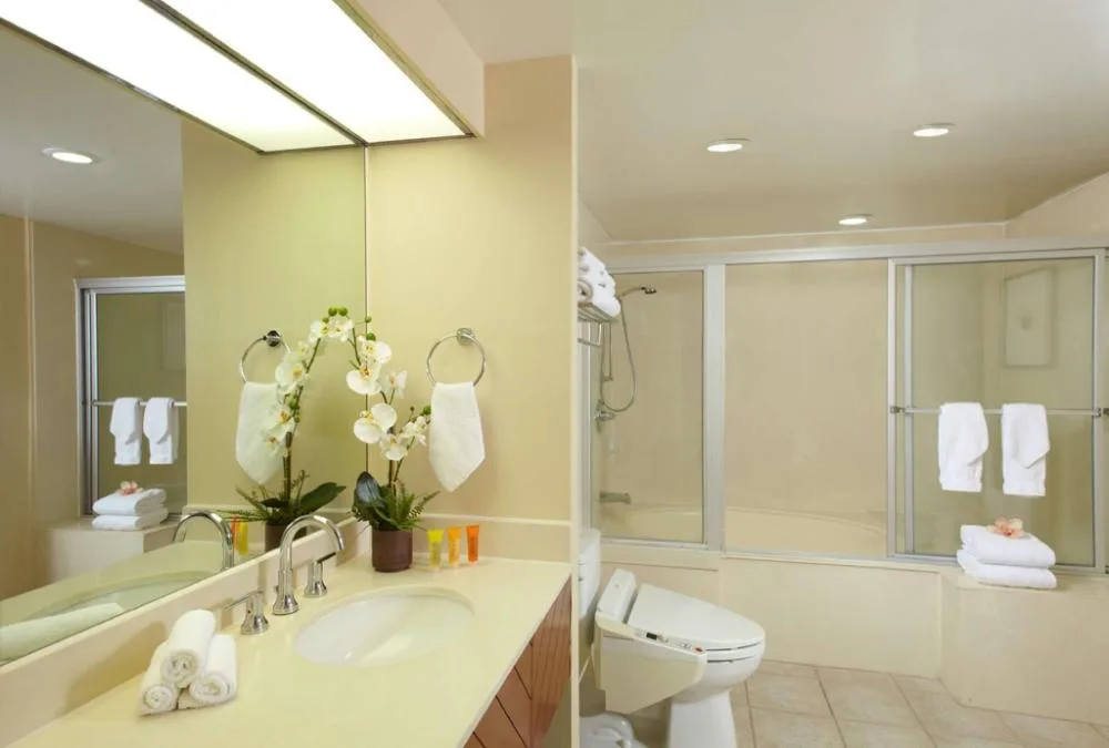 Bathroom with vanity, tub-shower and folded towels at Oasis Hotel Waikiki.
