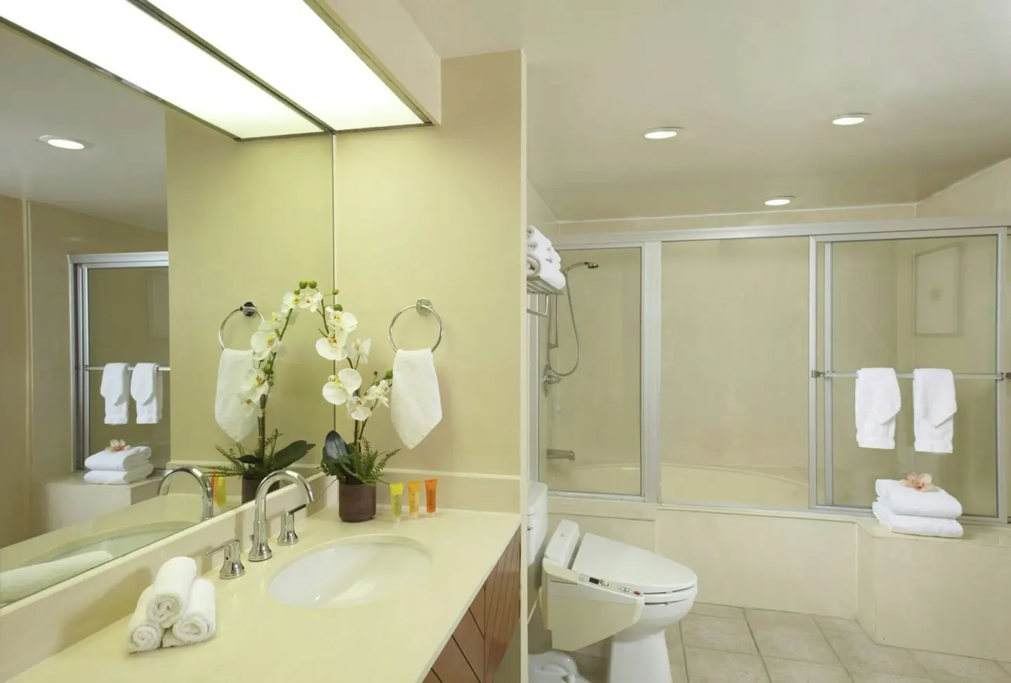 Standard Room bathroom vanity and tub-shower with folded towels at Oasis Hotel Waikiki.