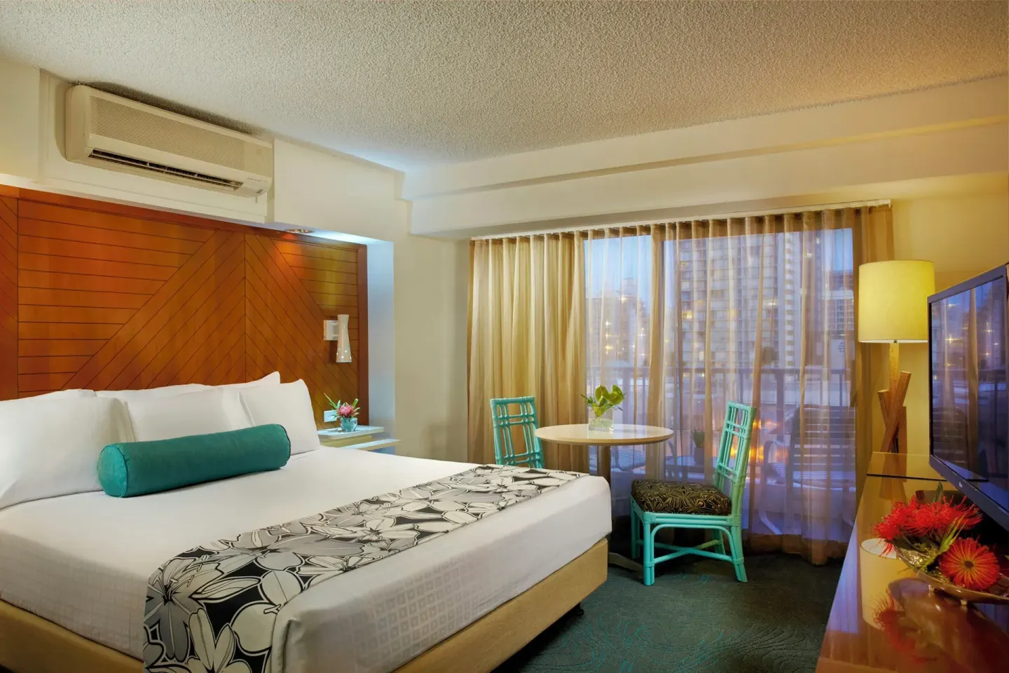 Standard Room with king bed, table, turquoise chairs and TV at Oasis Hotel Waikiki.