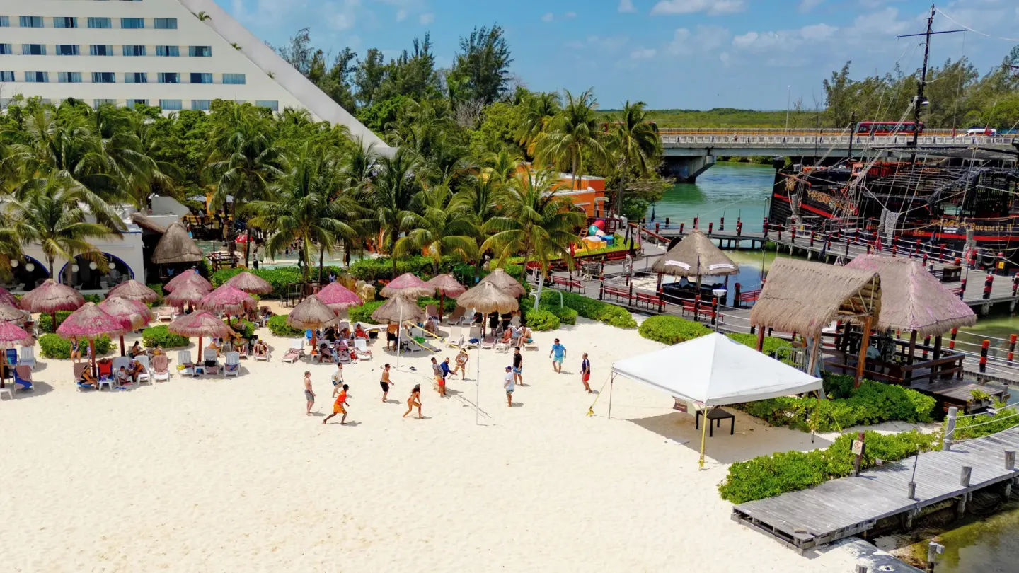 A sandy activity beach with palapas, loungers, and a dock at Oasis Palm.