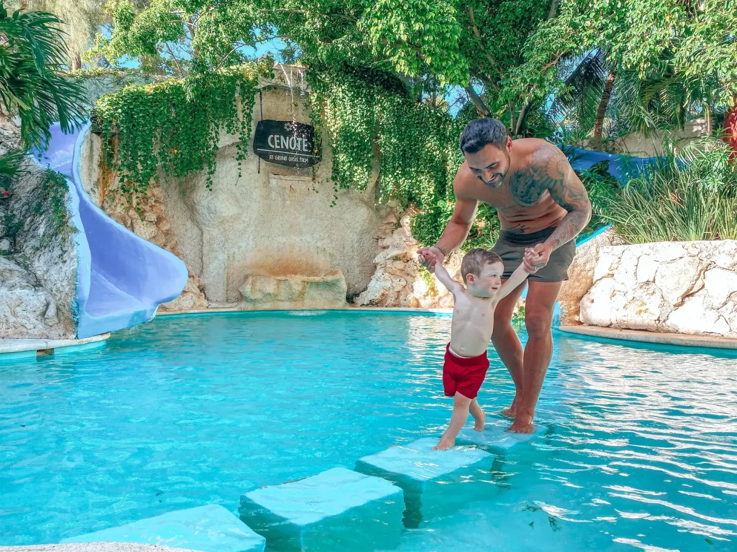 A parent helps a child cross floating steps in a pool at Oasis Palm.