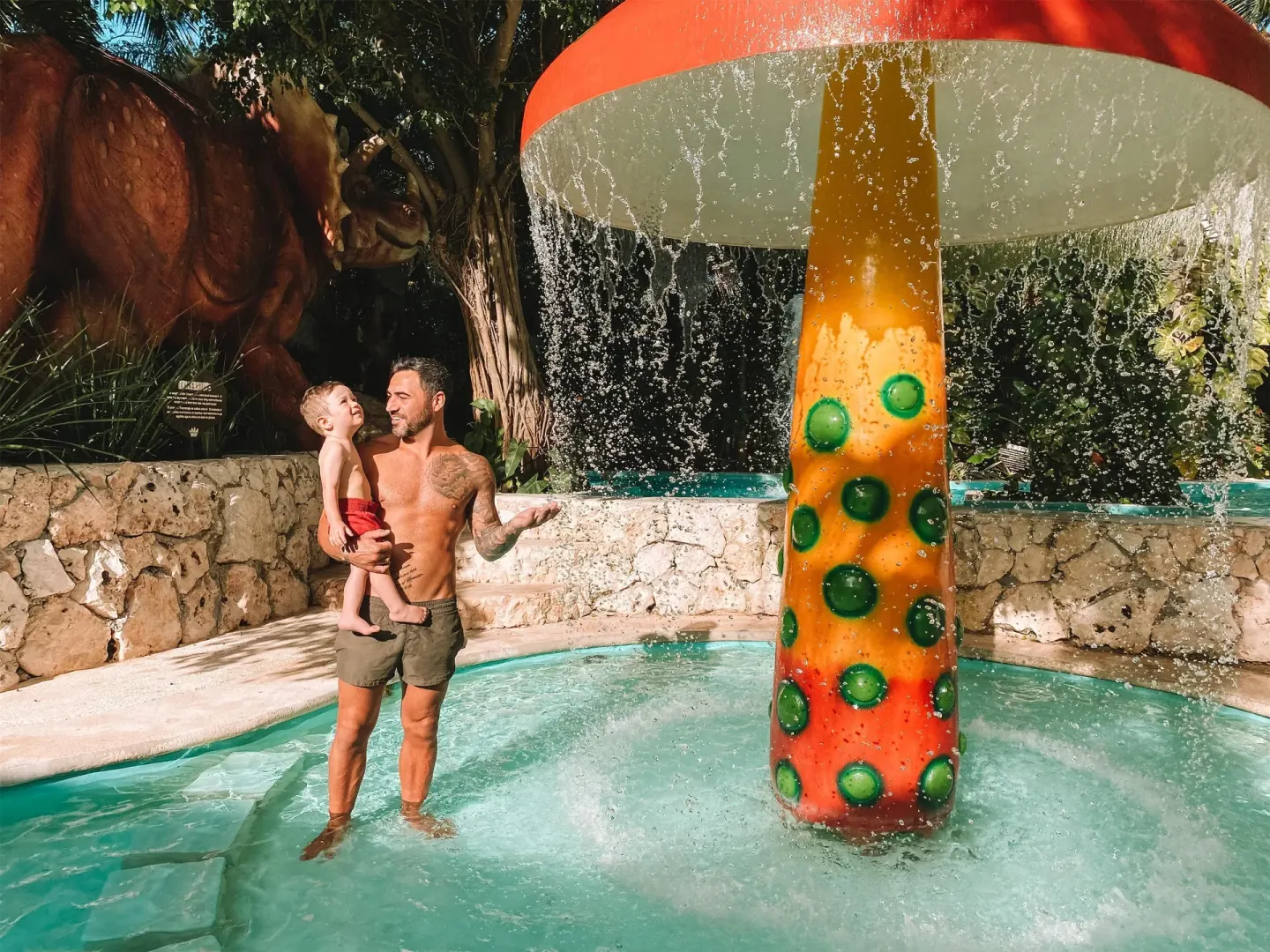 A man holds a child beside a mushroom water feature at Oasis Palm.