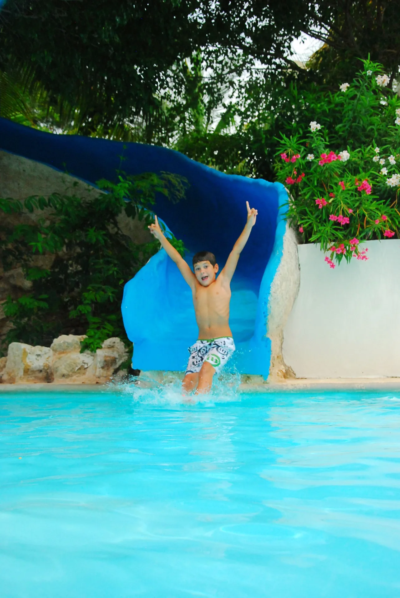 Child splashes into a pool from a curved blue water slide at Oasis Palm.