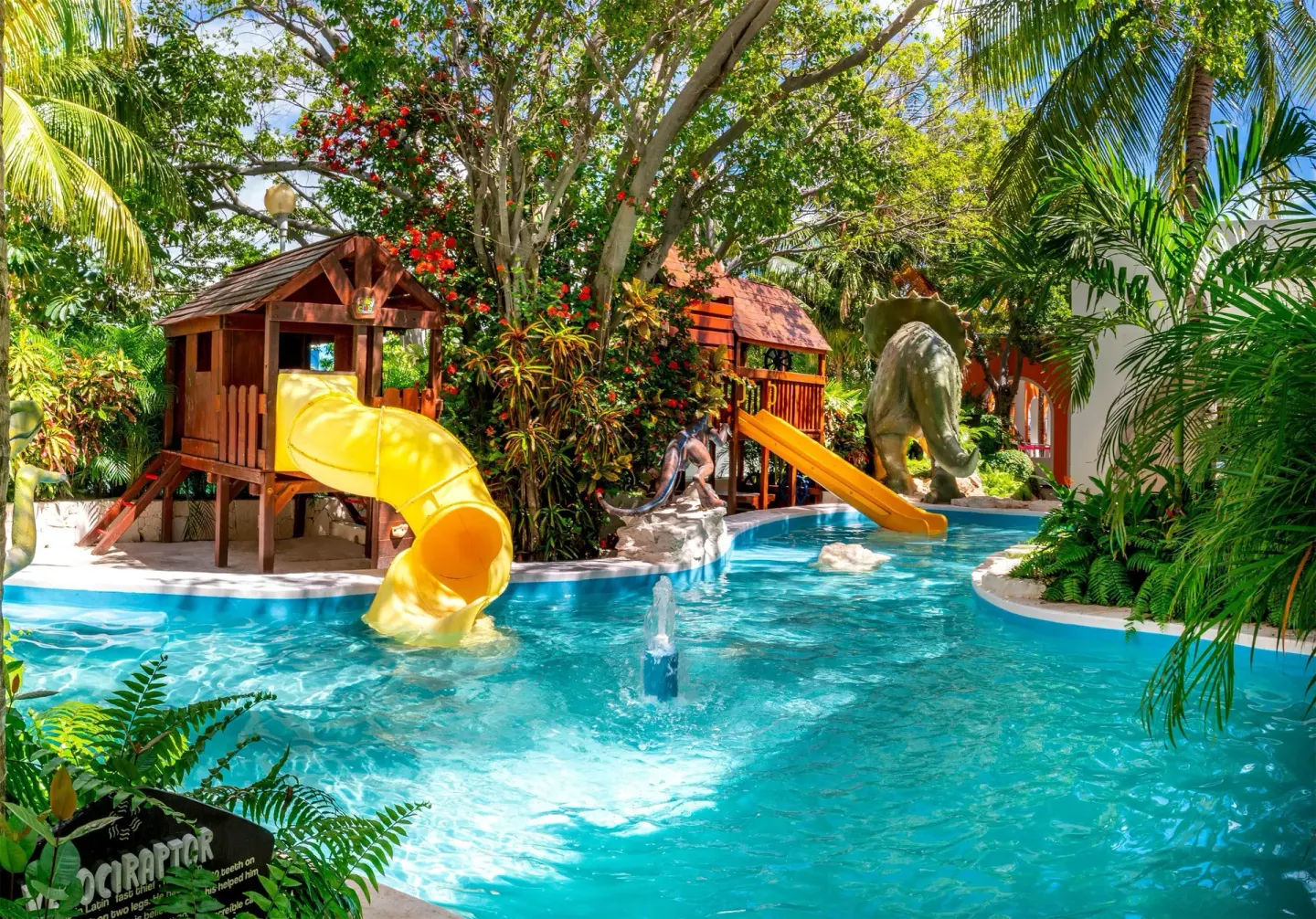 Kids' water play area with two slides, fountains, and dinosaur decor at Oasis Palm.