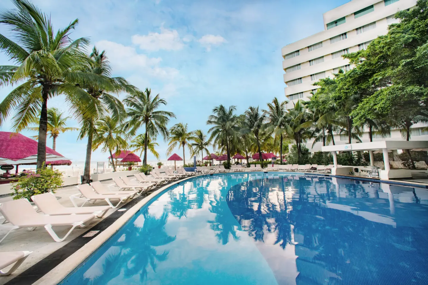 Large resort pool with lounge chairs, palms, and the hotel building at Oasis Palm.