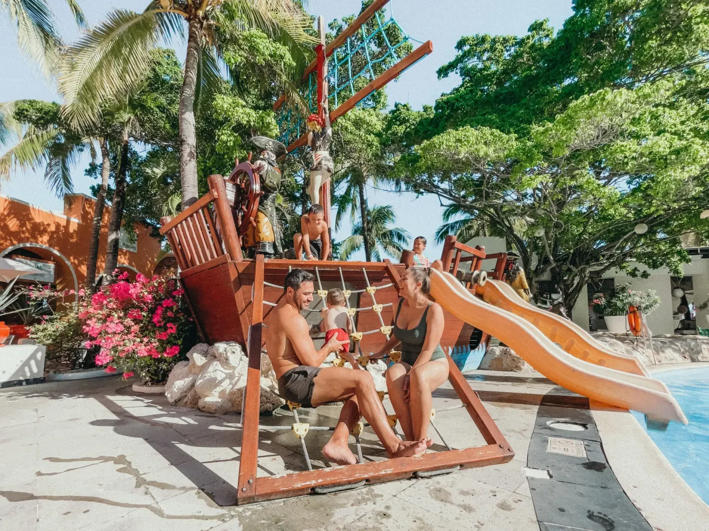 Families gather by a pirate ship play structure and pool slide at Oasis Palm.