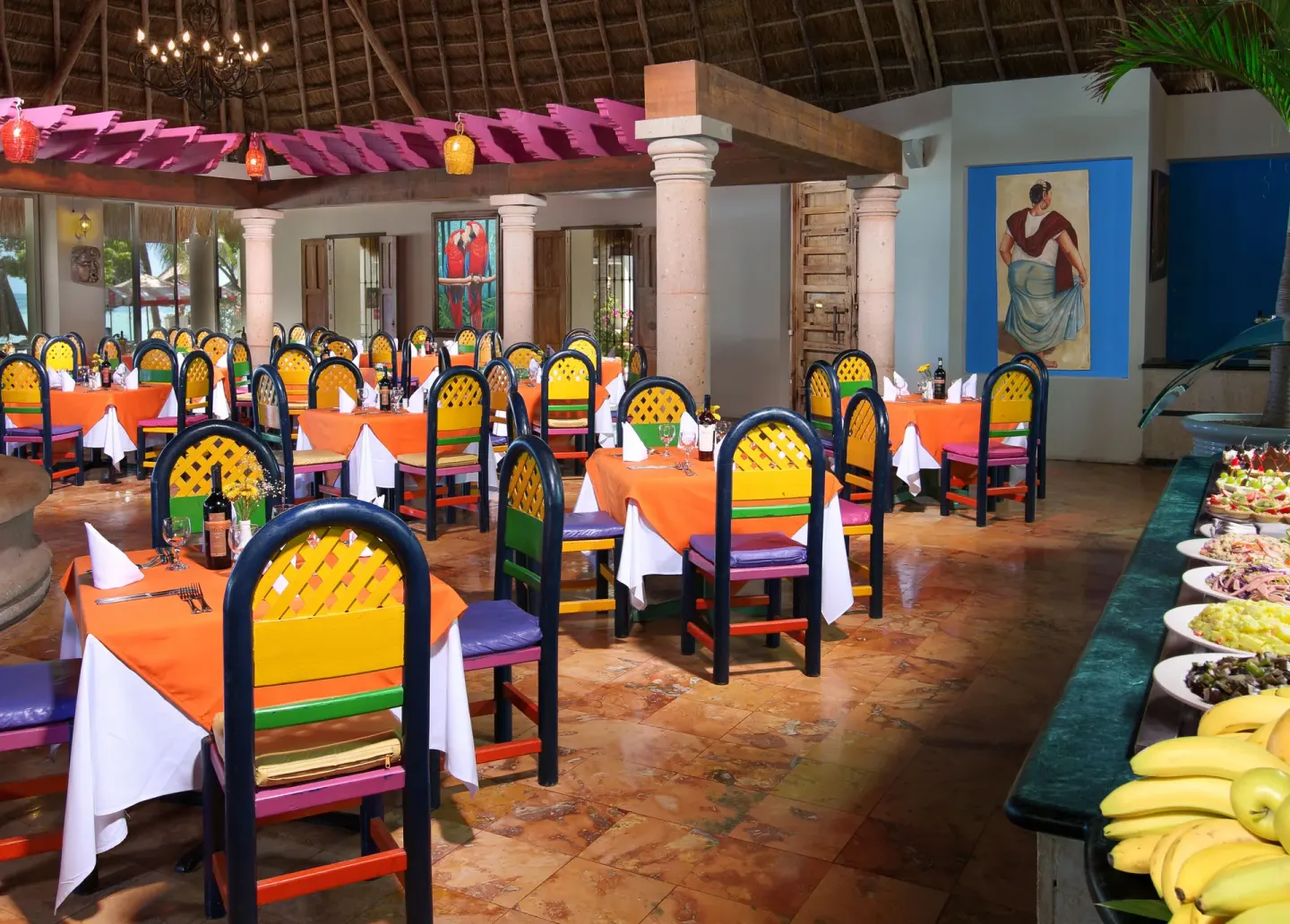 Dining room with colorful chairs, orange tablecloths, and buffet display at Oasis Palm.