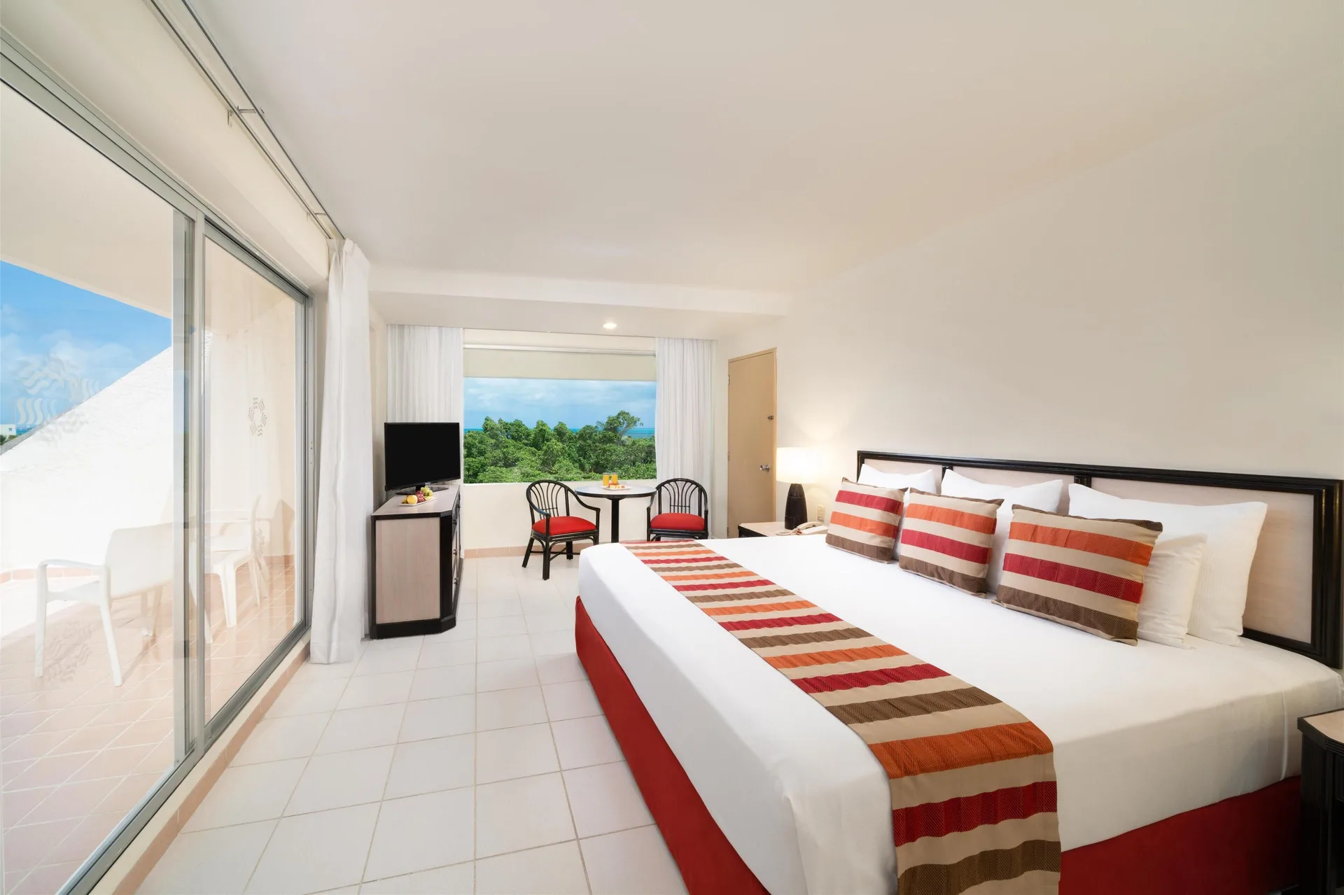Family room at Oasis Palm with a king bed, balcony doors, seating area, and greenery beyond the window.