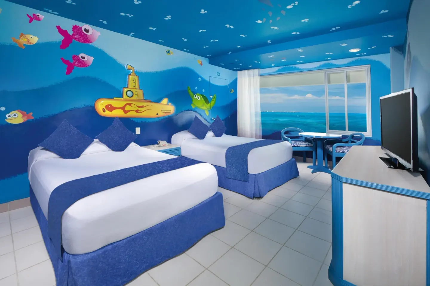 Family room at Oasis Palm with two double beds, ocean-themed murals, seating, and a TV.