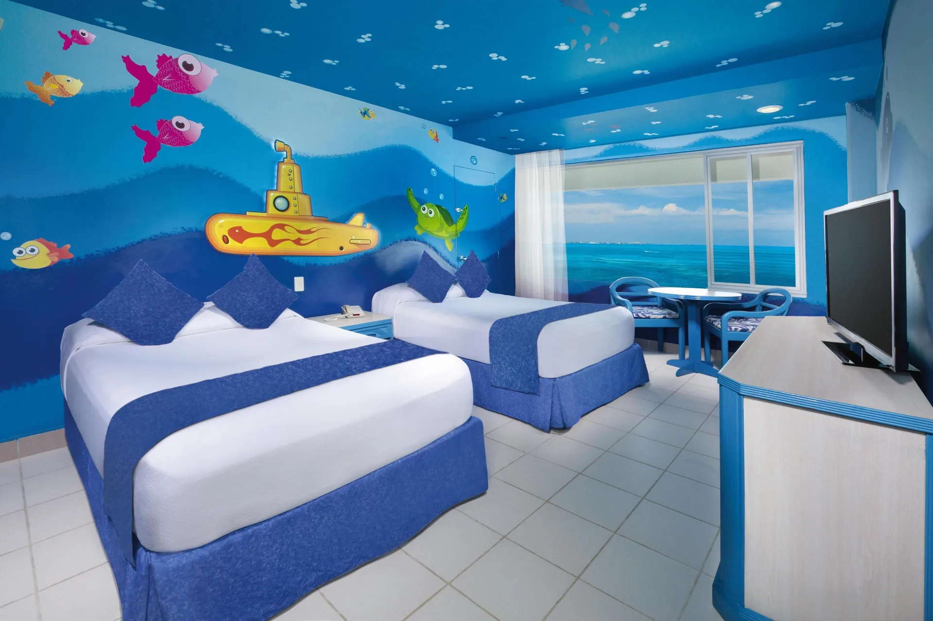 Family room at Oasis Palm with two double beds, ocean-themed murals, seating, and a TV.