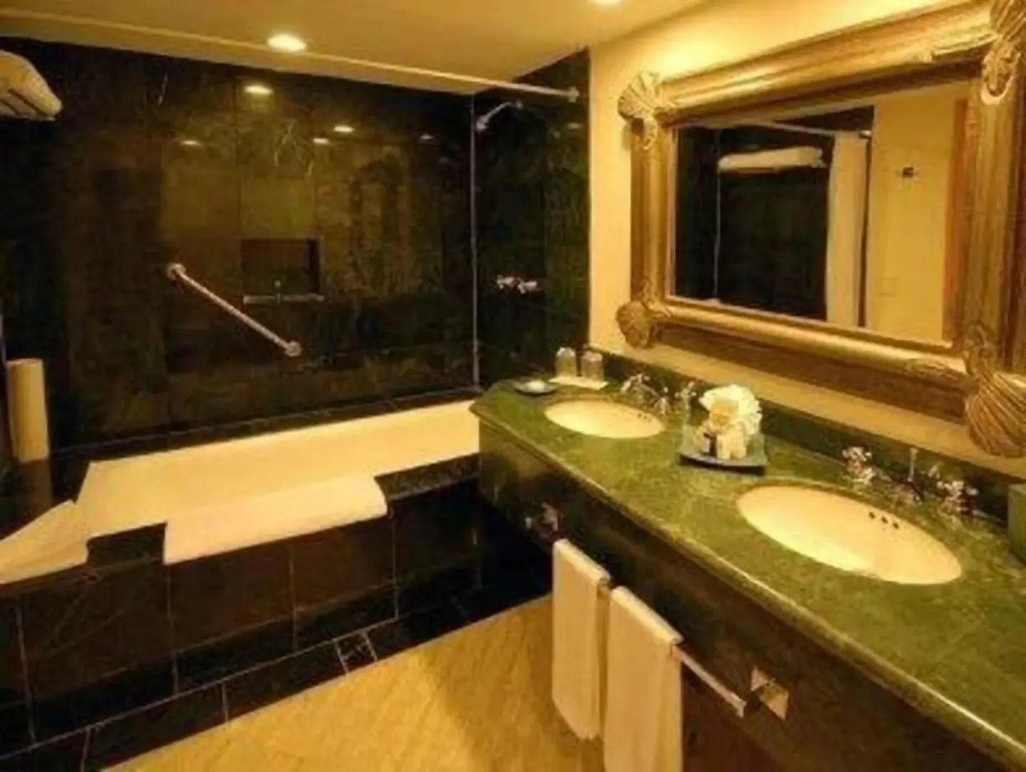 Standard Room bathroom at Oasis Palm with double sinks, green countertop, bathtub, mirror, and dark tile.