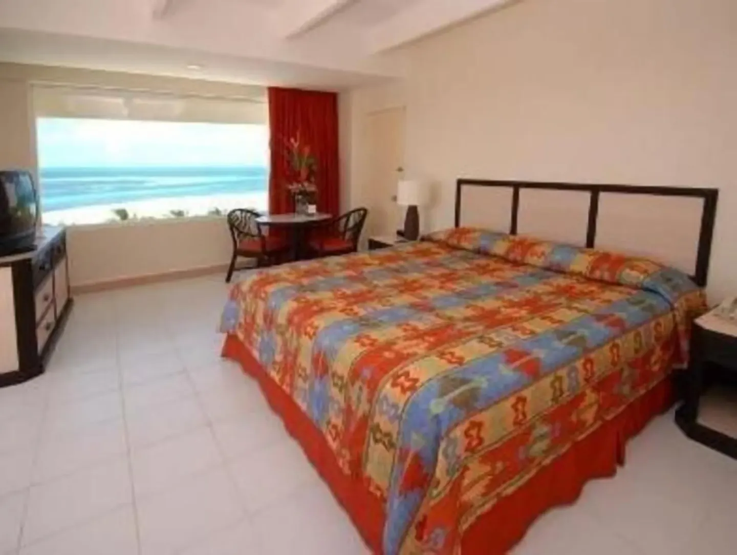 Standard Room at Oasis Palm with a large bed, colorful bedding, TV, seating area, and ocean view.
