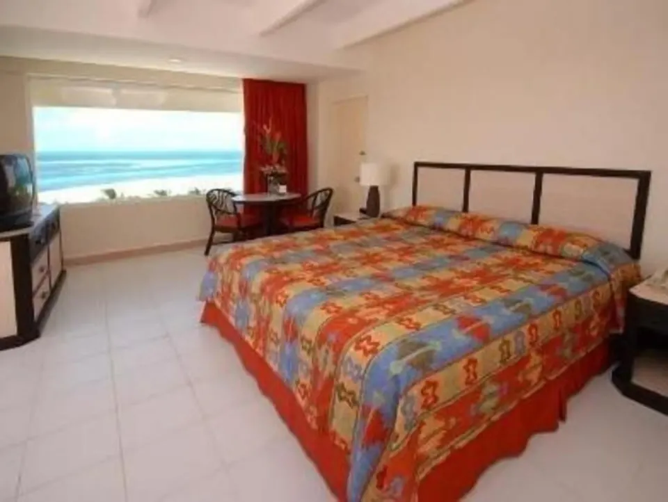 Standard Room at Oasis Palm with a large bed, colorful bedding, TV, seating area, and ocean view.