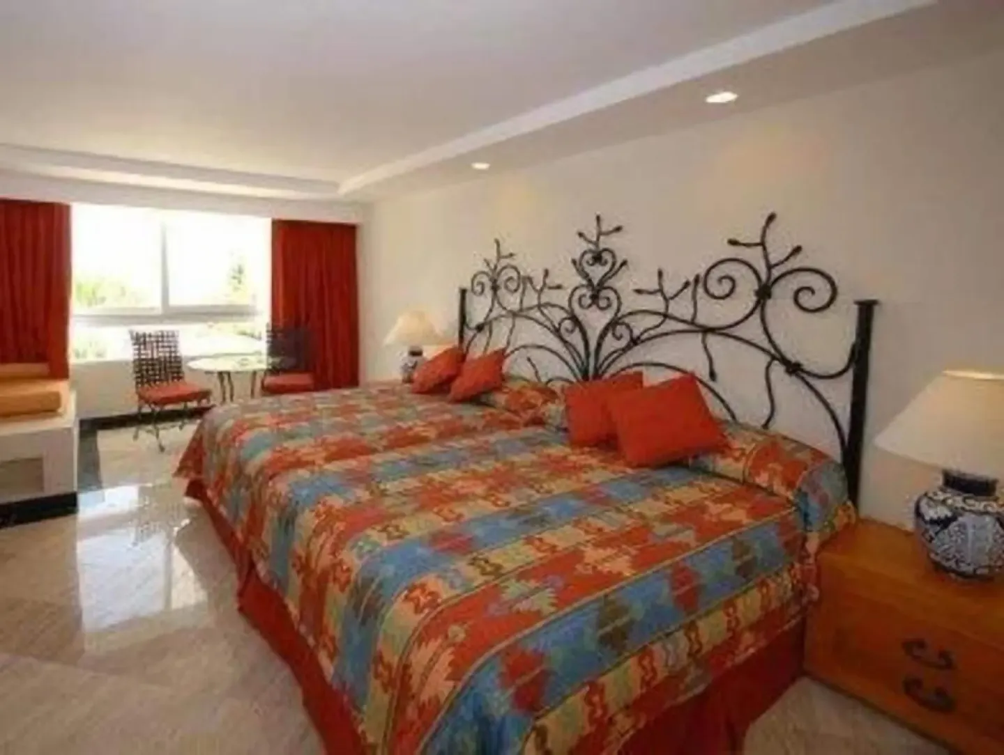 Standard Room at Oasis Palm with two beds, ornate metal headboards, colorful bedding, and red curtains.